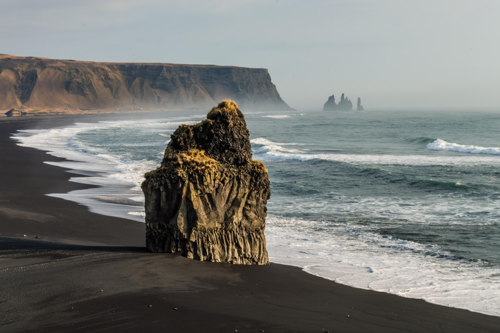 Reynisfjara Beach in Island mit tiefschwarzem Lavasand, steilen Klippen und nebliger Meereskulisse.