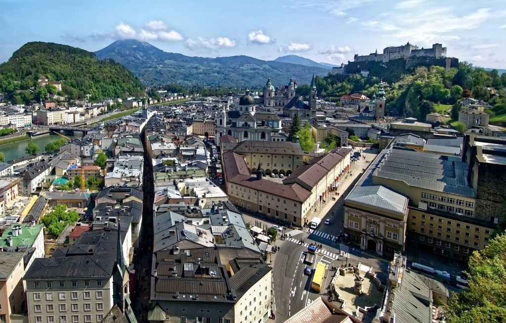 Panoramablick auf Salzburg mit der Festung Hohensalzburg über der historischen Altstadt, umgeben von barocken Gebäuden und den Alpen im Hintergrund.
