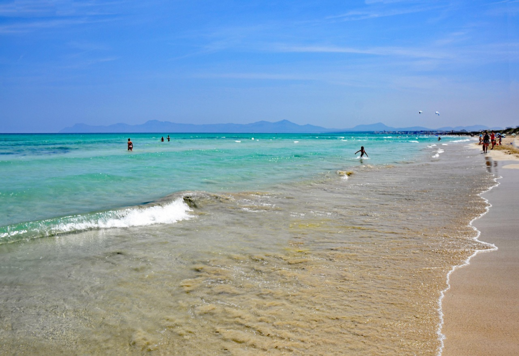 Strandlandschaft der Playa de Muro: breiter Sandstrand, seichtes Wasser und ruhige Mittelmeer Atmosphäre.